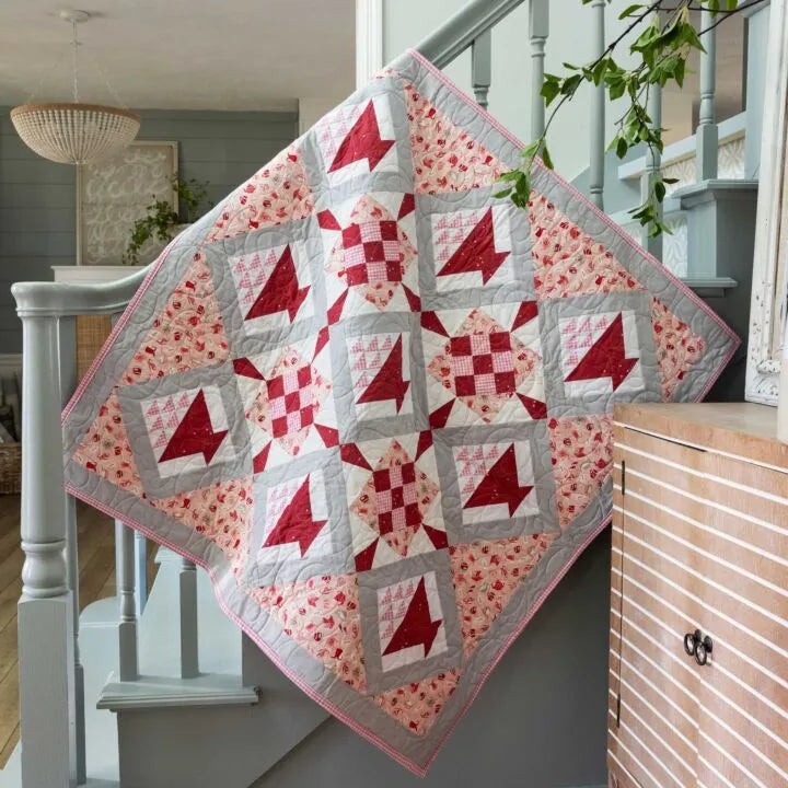 Basket and 9 patch star quilt made with teacup themed fabrics draped over a picnic basket outdoors